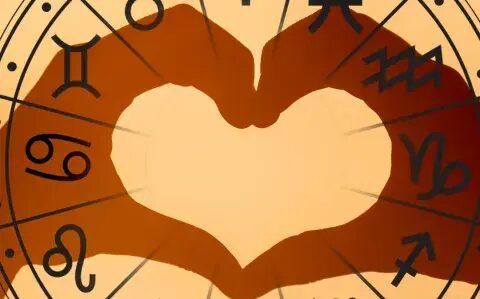 Dos manos formando un corazón sobre la rueda del zodiaco