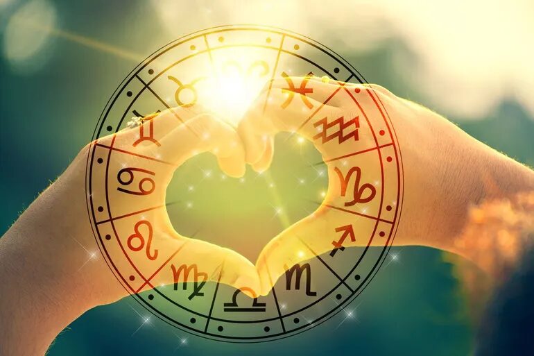 Dos manos formando un corazón sobre la rueda del zodiaco